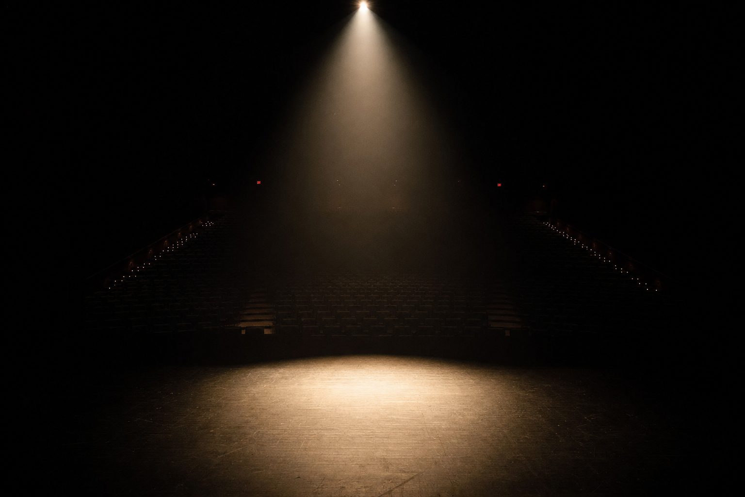 An empty stage under a single warm spotlight in a dark auditorium